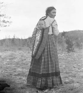 First Nation woman with a baby on a cradleboard on her back.