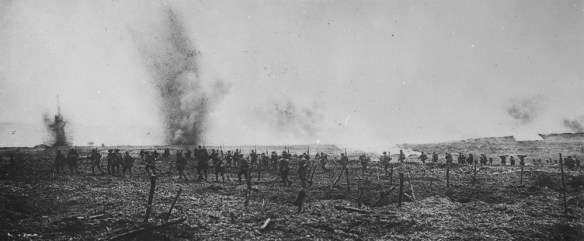 Group of men going through barbed wire with shells exploding in the background.
