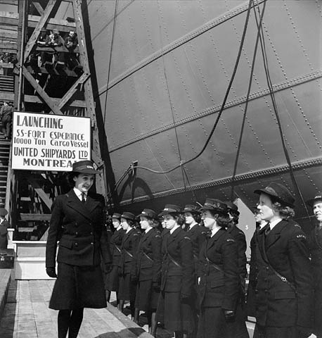 A group of women standing at attention next to the hull of a cargo ship.