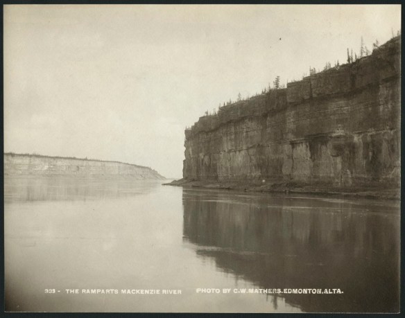Black and white photograph of a river with vertical flat cliffs on the right side. The top layer of the cliffs holds trees and vegetation. To the left side and further off in the distance is a similar geological feature. The river runs between the two features.