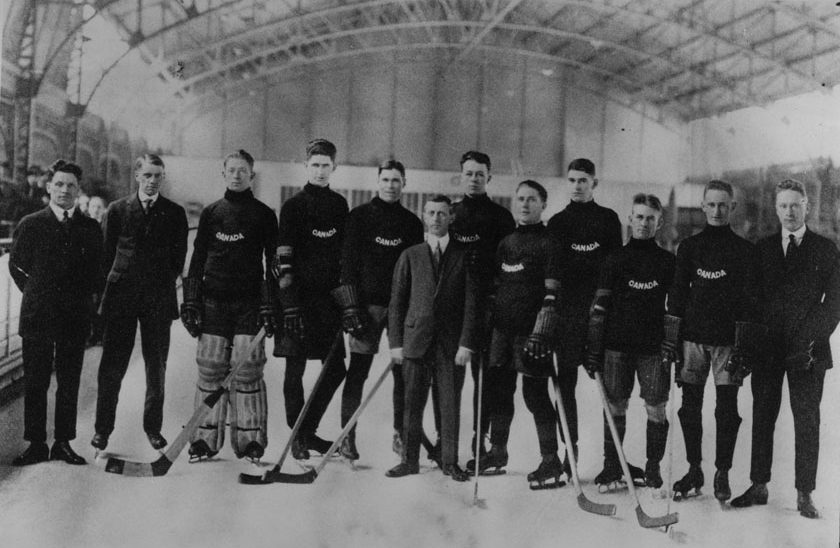 A black and white photograph of a men’s hockey team standing on the ice holding hockey sticks.