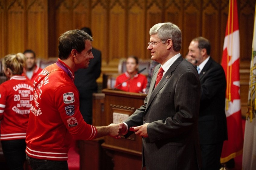 Photograph of two men smiling and shaking hands.