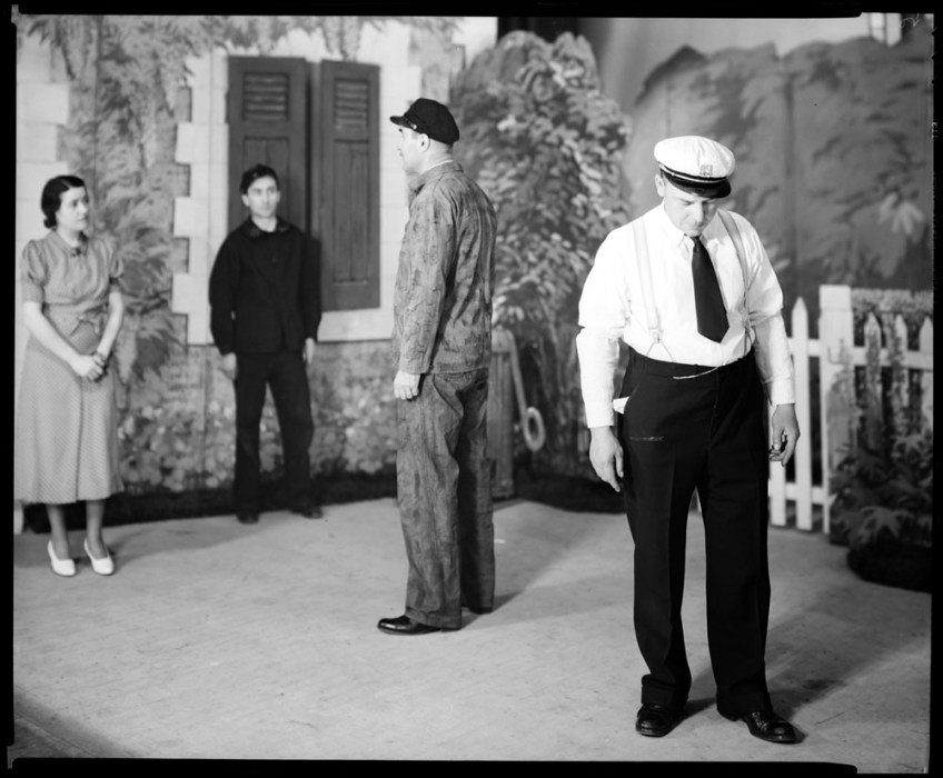 Photograph of four people standing on a stage in the middle of a set.