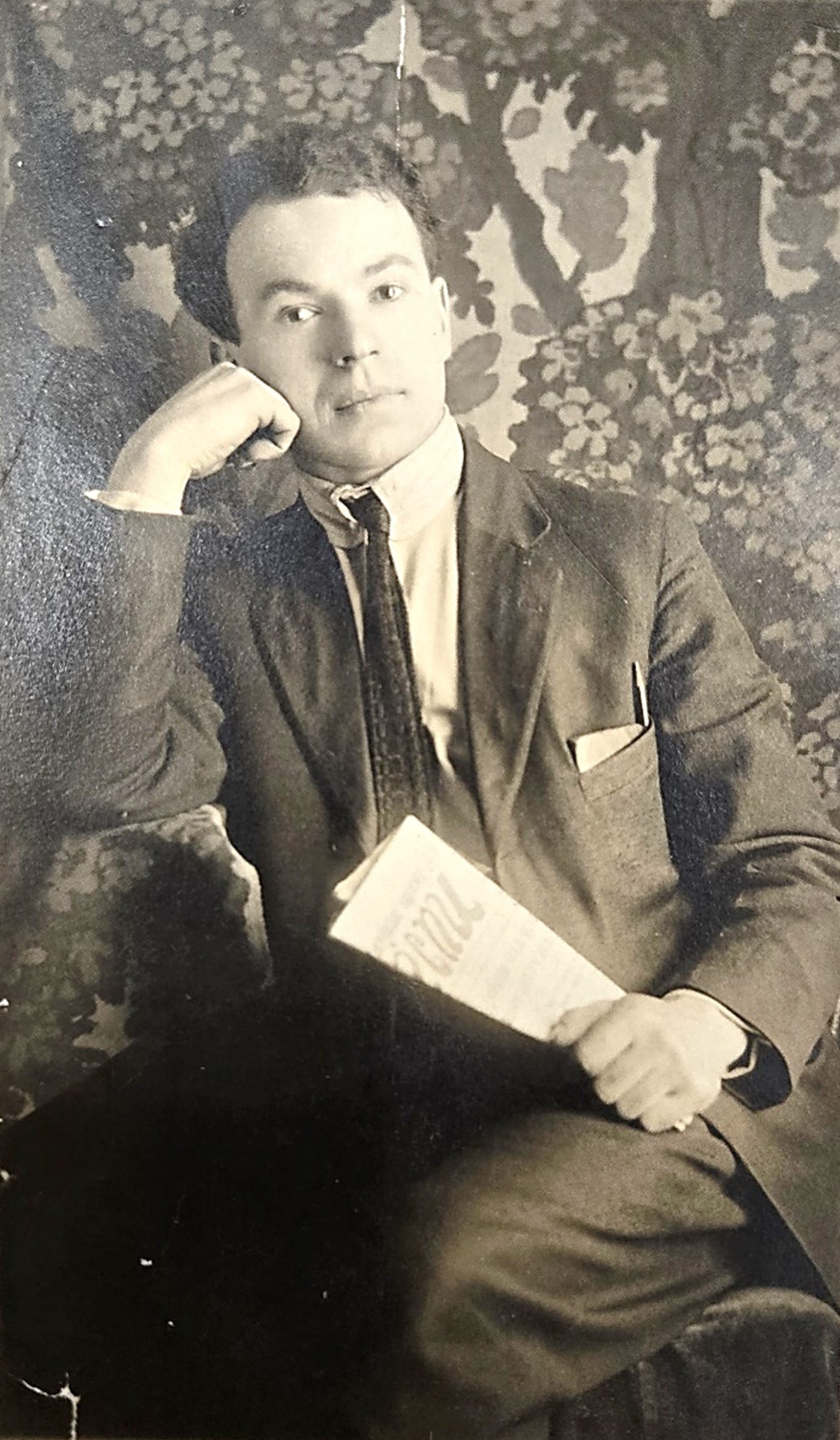 Studio portrait of a seated man. He is holding a newspaper.